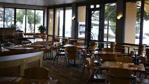 A restaurant with a wooden interior, large windows, and a counter with a plant.