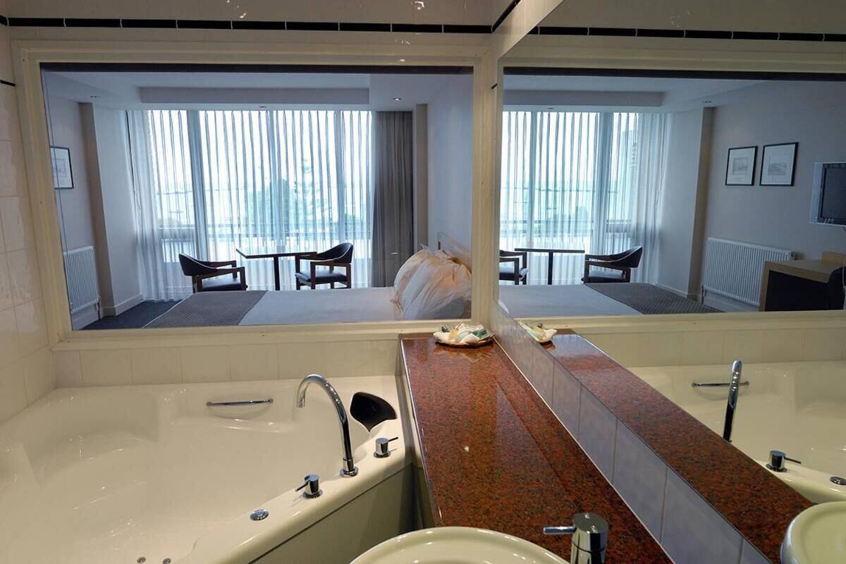 A hotel bathroom with a large mirror, a bathtub, a sink, and a vanity.