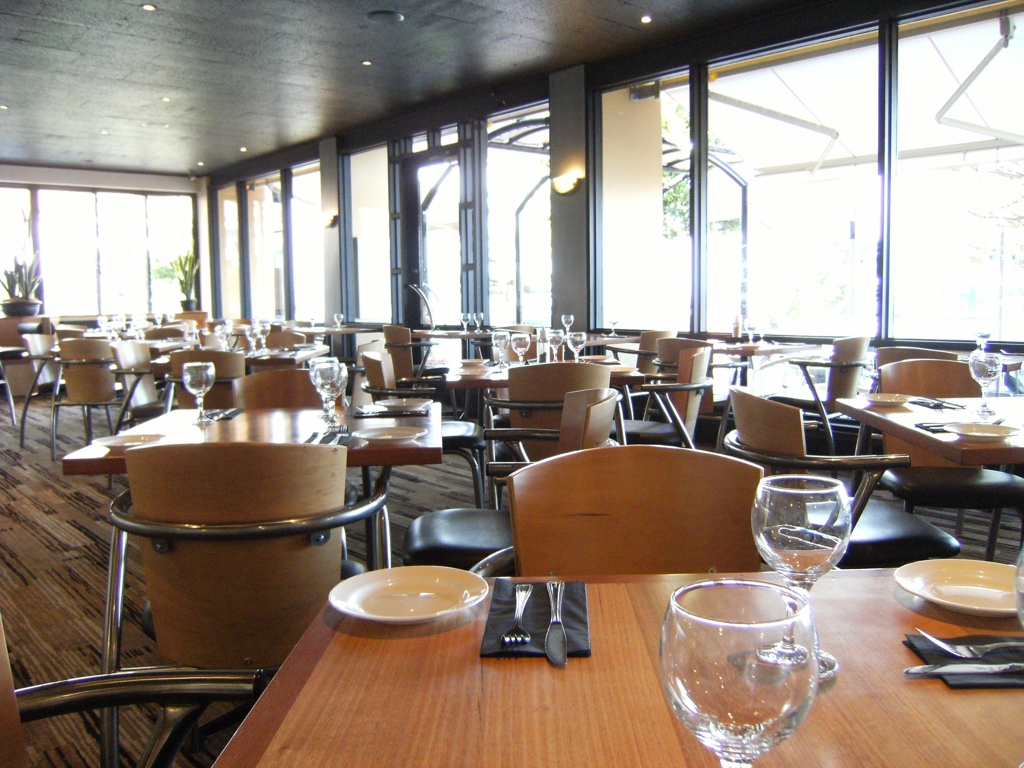 A spacious restaurant with multiple tables and chairs, large windows, and a modern interior design.