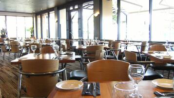 A spacious restaurant with multiple tables and chairs, large windows, and a modern interior design.