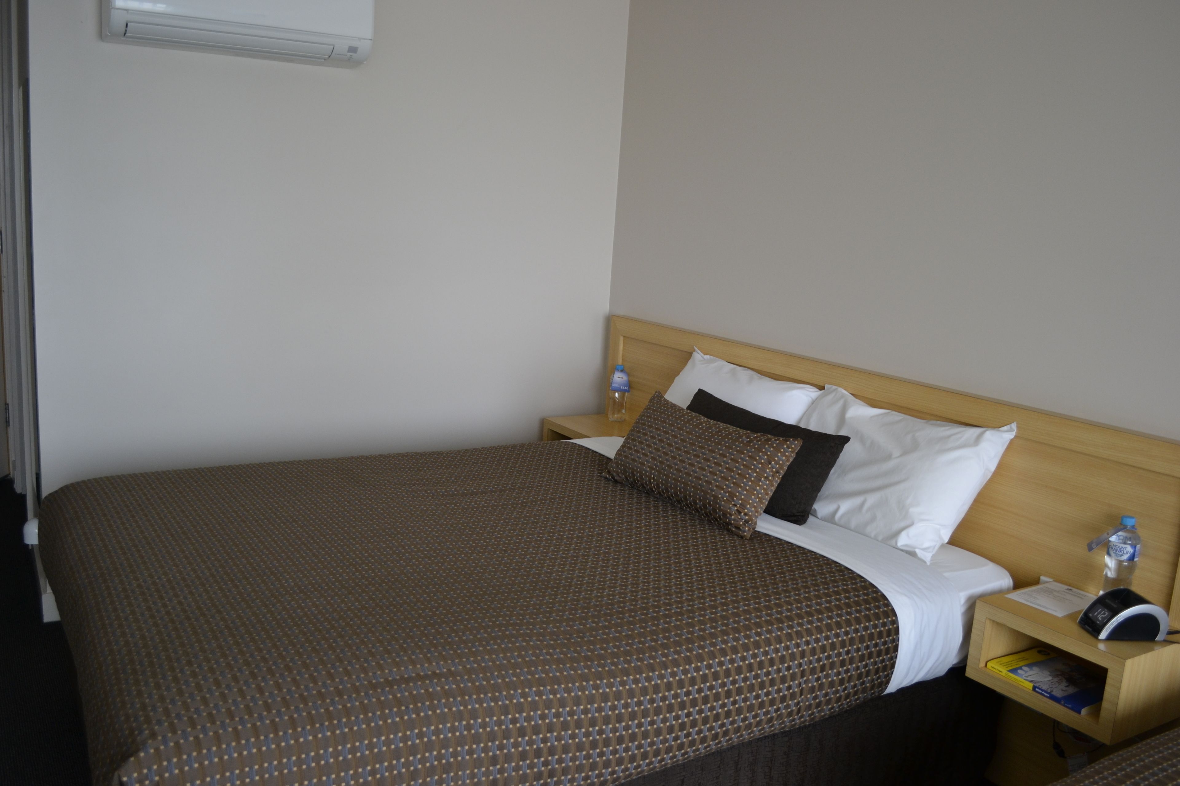 A neatly made bed with a patterned bedspread, a wooden headboard, and a bedside table with a water bottle and a book.