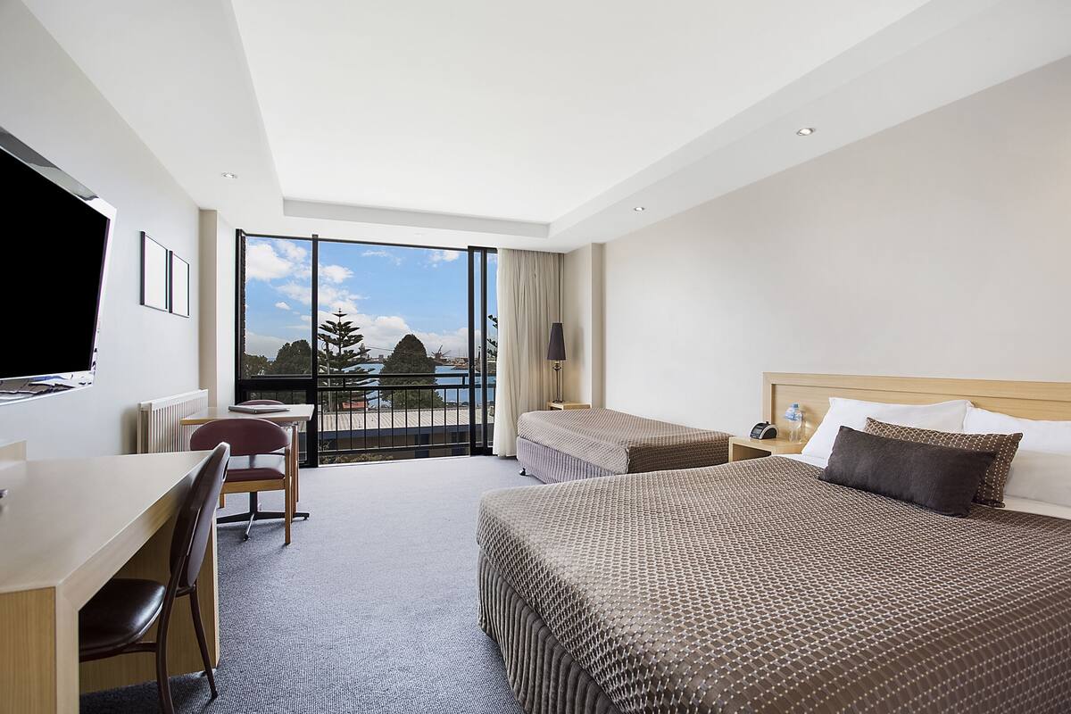 A hotel room with a large bed, a desk, a chair, and a view of the outdoors.