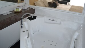 A bathroom with a large bathtub, a mirror, and a counter with toiletries.