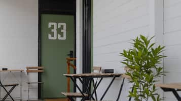 A small outdoor seating area with tables and chairs, a green door with the number 33, and a potted plant.