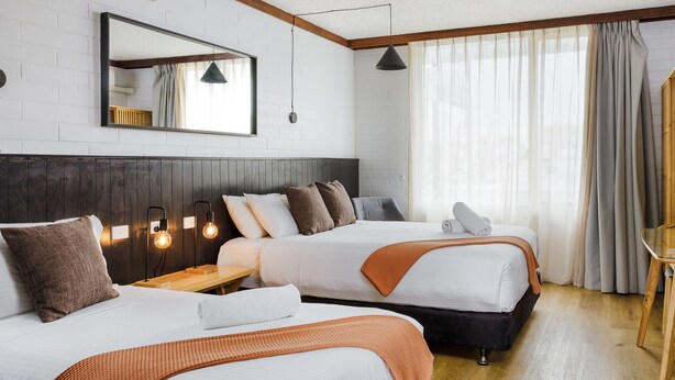 A hotel room with two beds, a wooden headboard, a large mirror, and a window with curtains. - m. hotel (Sale)