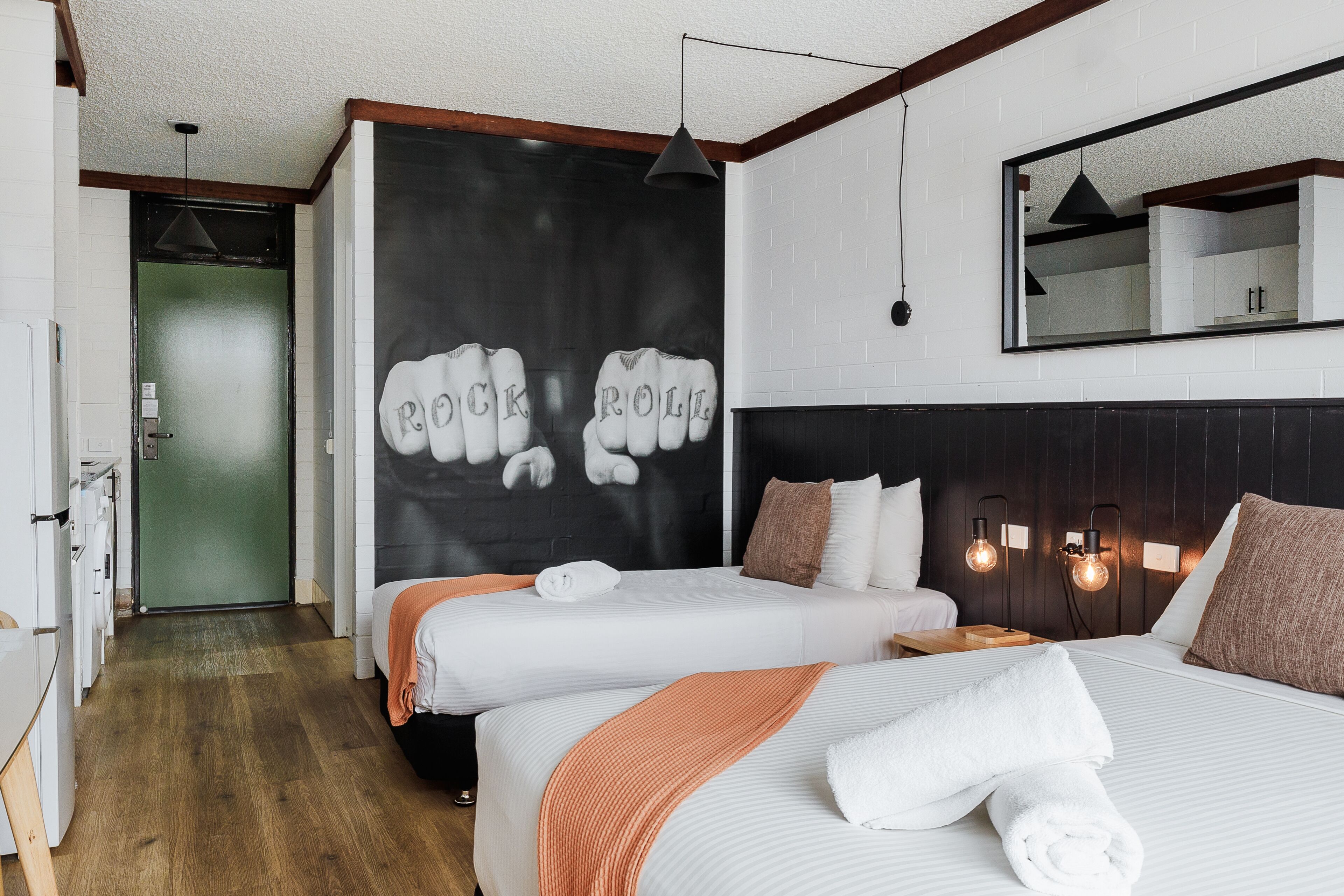 A hotel room with two beds, a large mirror, a wall-mounted light fixture, and a door leading to a bathroom.