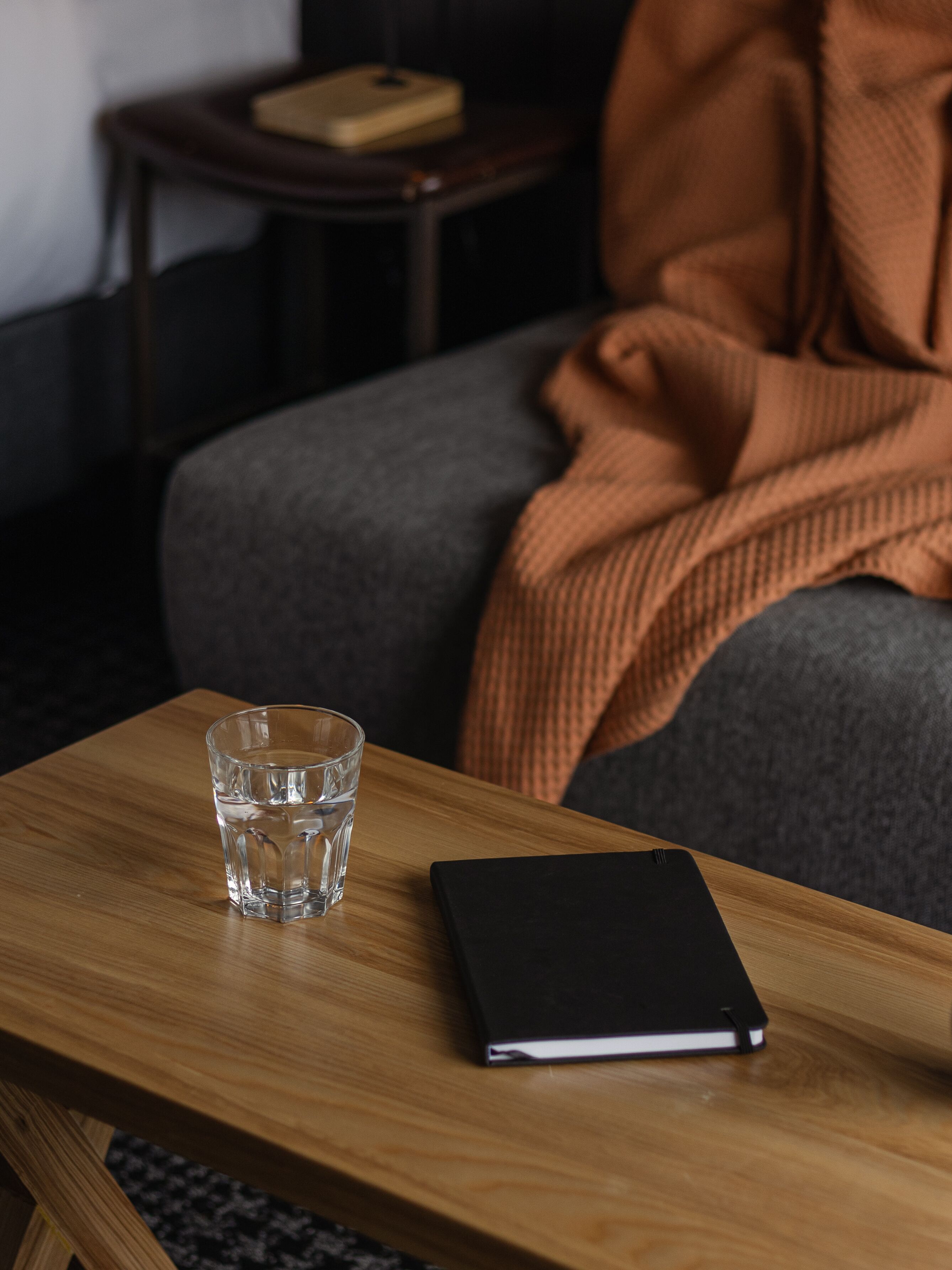 A wooden table with a glass of water and a black notebook.