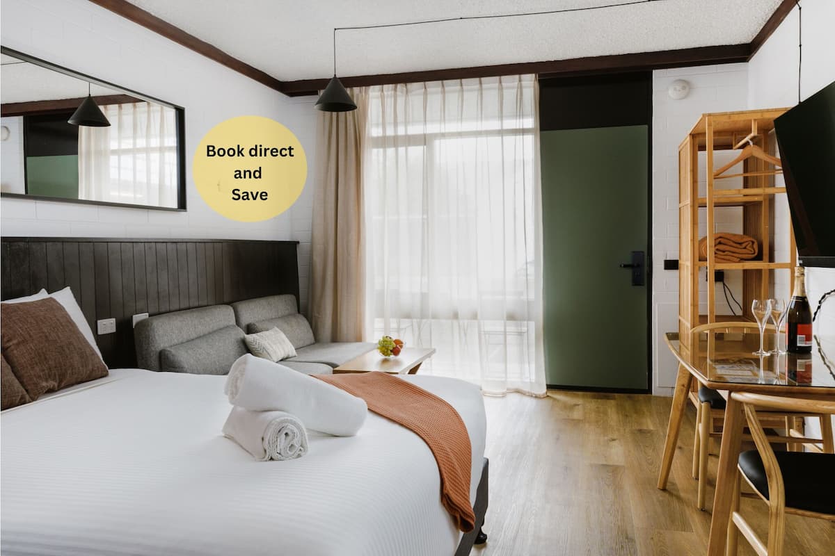 Habitación de hotel con una cama grande, un escritorio, una silla, un televisor y un armario.