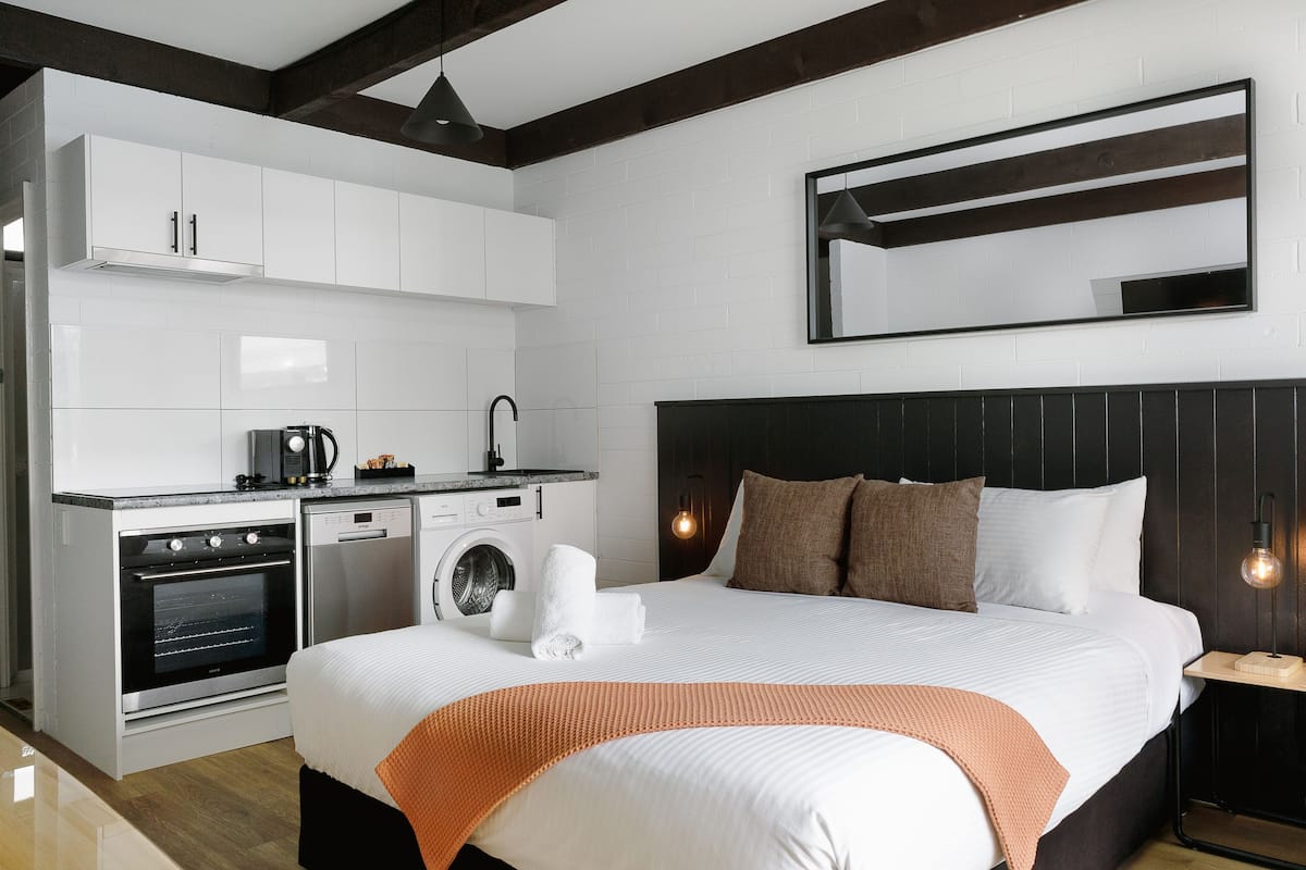 Una habitación de hotel moderna con una cama grande, lavadora integrada y una kitchenette.