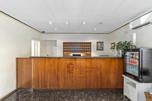 A reception area with a wooden counter, a framed picture above it, and a refrigerator with beverages. - Sherbourne Terrace Hotel (Shepparton)