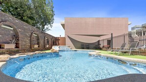 Ein Pool mit Backsteinmauer, ein modernes Gebäude und Außenbereich mit Sitzmöglichkeiten.