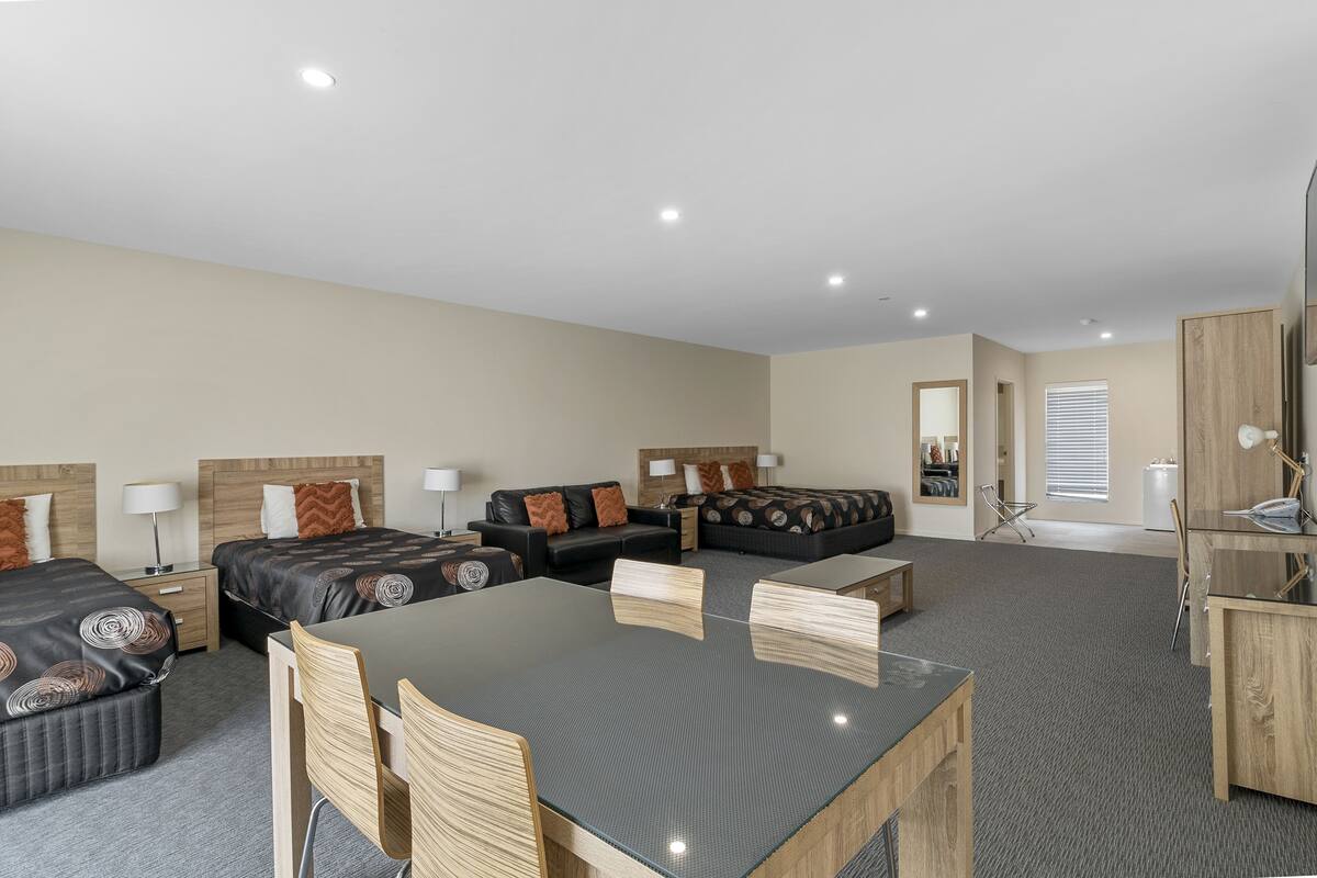 A hotel room with two beds, a dining table, and a sofa.