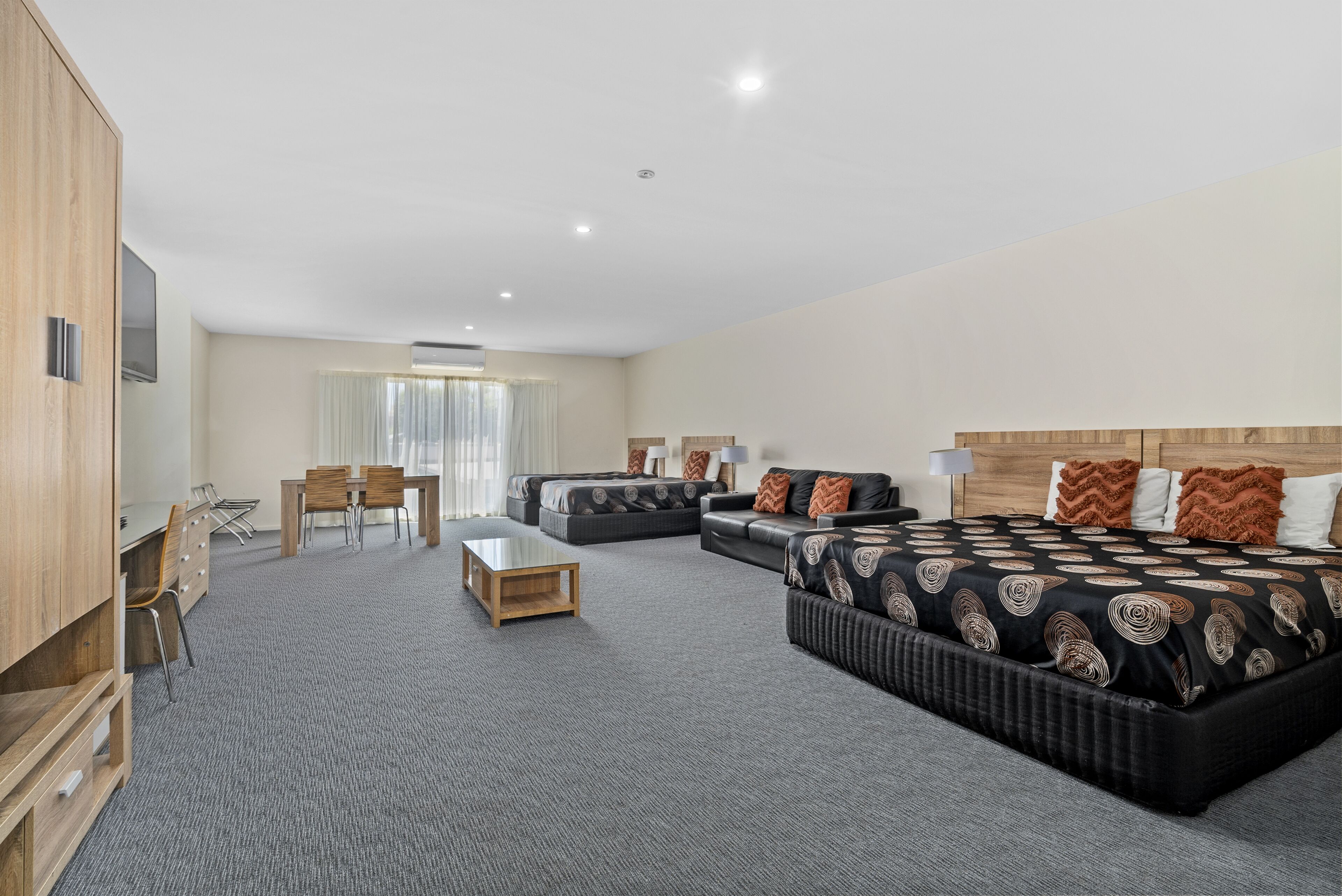 A modern hotel room with a large bed, a sofa, a dining area, and a TV.