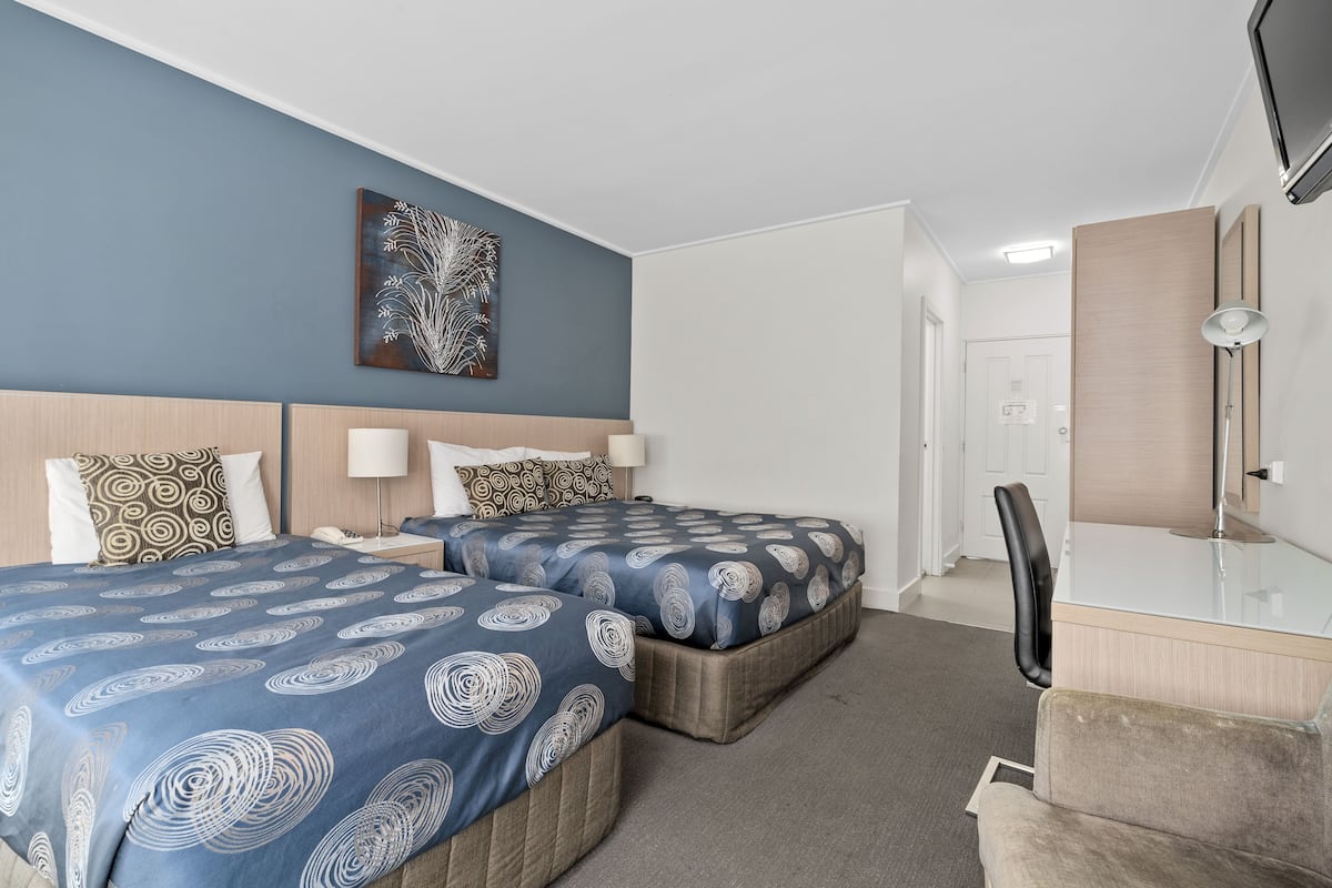 A hotel room with two beds, a desk, a chair, a mirror, and a wall-mounted TV.