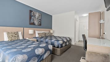 A hotel room with two beds, a desk, a chair, a mirror, and a wall-mounted TV.