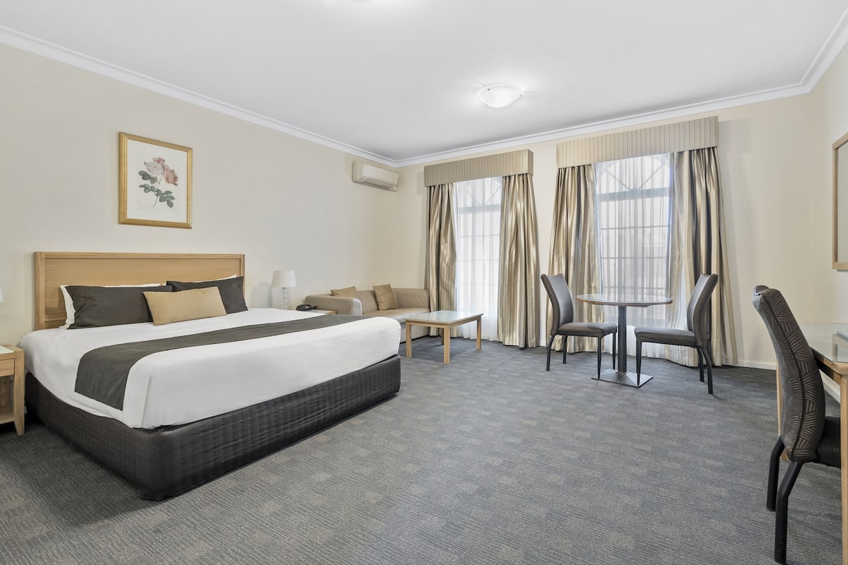 A hotel room with a large bed, a sofa, a small table, and two chairs.