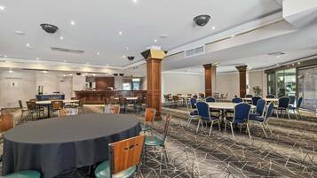 Un salón de conferencias de hotel con mesas redondas, sillas azules y piso alfombrado.