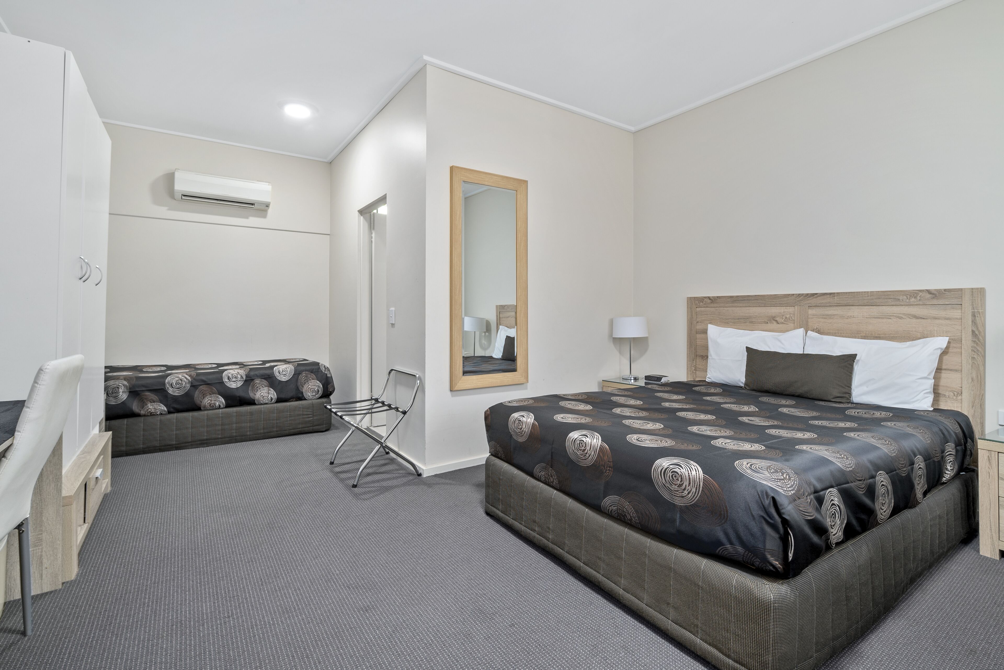 A hotel room with a large bed, a smaller sofa, a desk, and a chair.