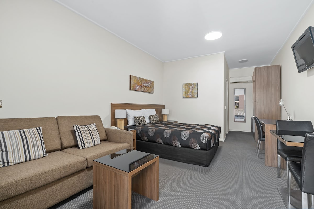A hotel room with a bed, a sofa, a desk, and a TV.
