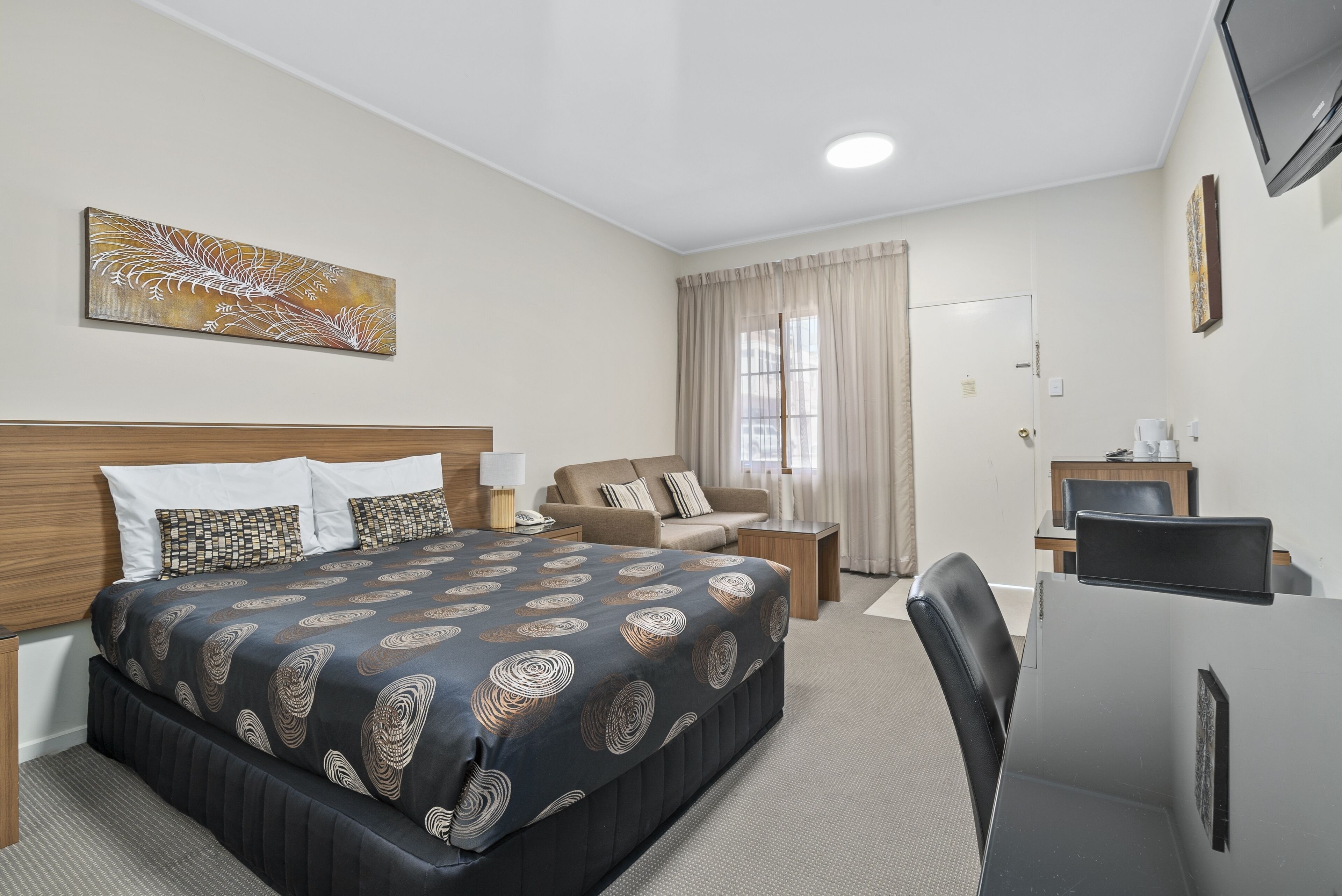 A hotel room with a large bed, a desk with a computer, a sofa, and a TV.