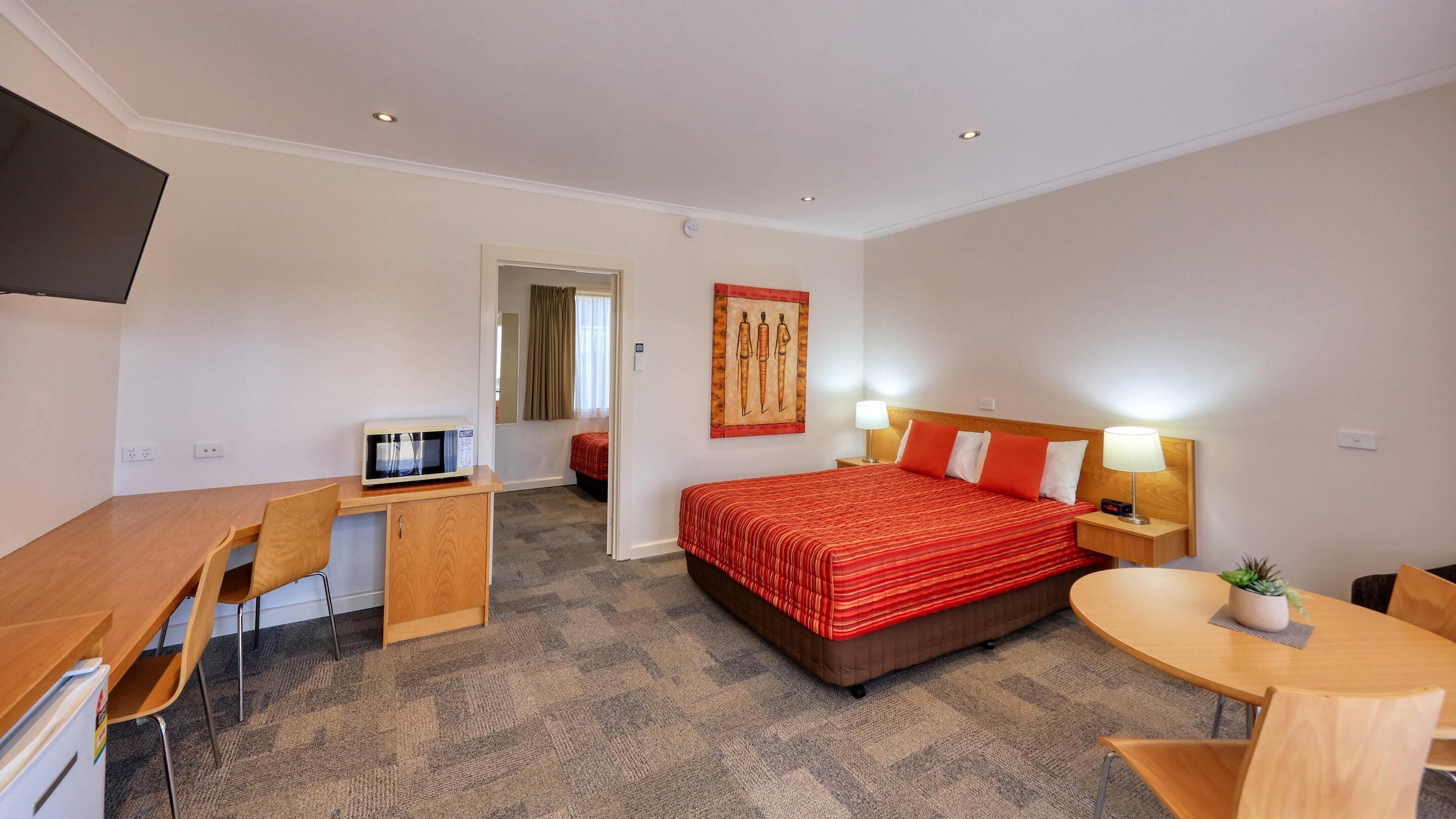 A hotel room with a bed, desk, chair, and a small table with a plant.