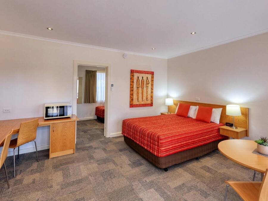 A hotel room with a bed, desk, chair, and a small table with a plant.