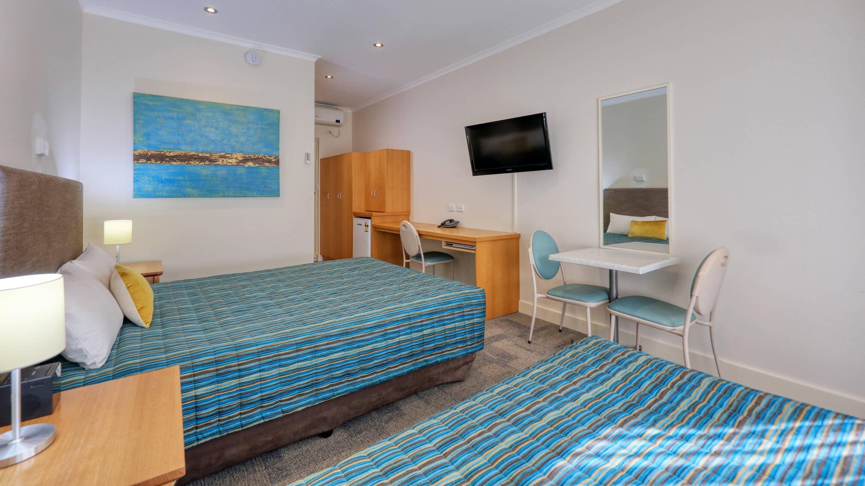 A hotel room with two beds, a desk, a chair, a television, and a painting on the wall.