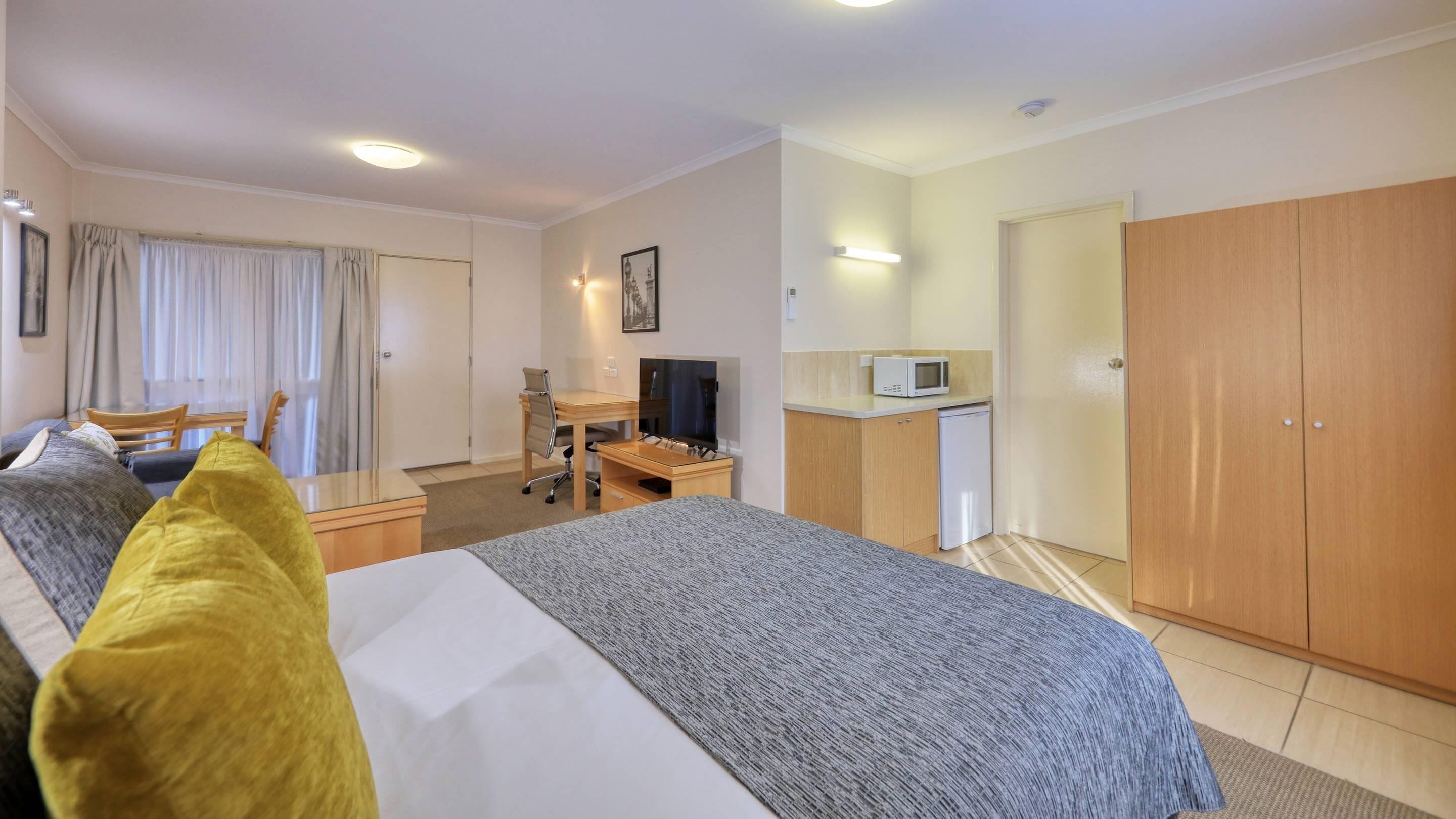 Hotellihuone, jossa on sänky, työpöytä, jossa on televisio, mikroaaltouuni ja vaatekaappi.