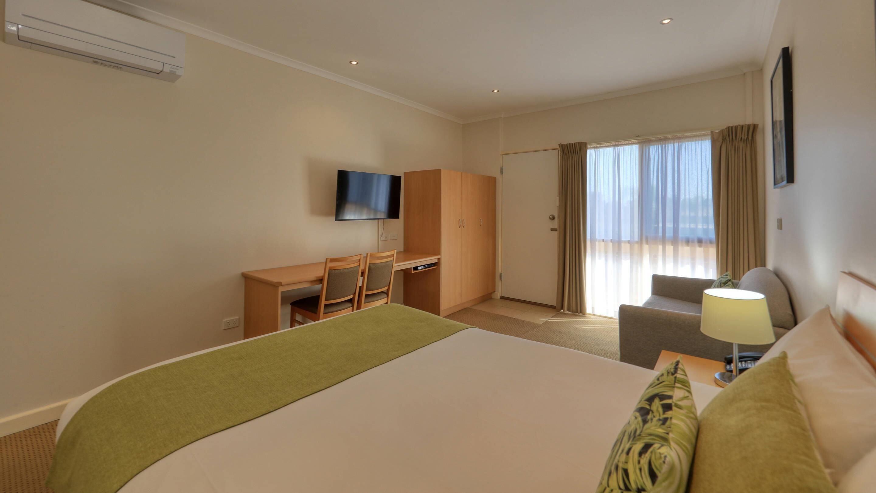 A hotel room with a bed, a desk, a chair, a TV, and a window with curtains.