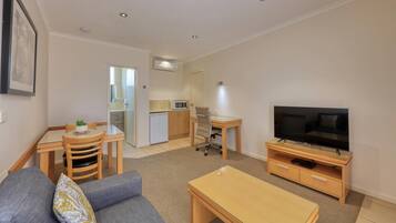 A compact living space with a sofa, a TV, a dining table, and a kitchenette.
