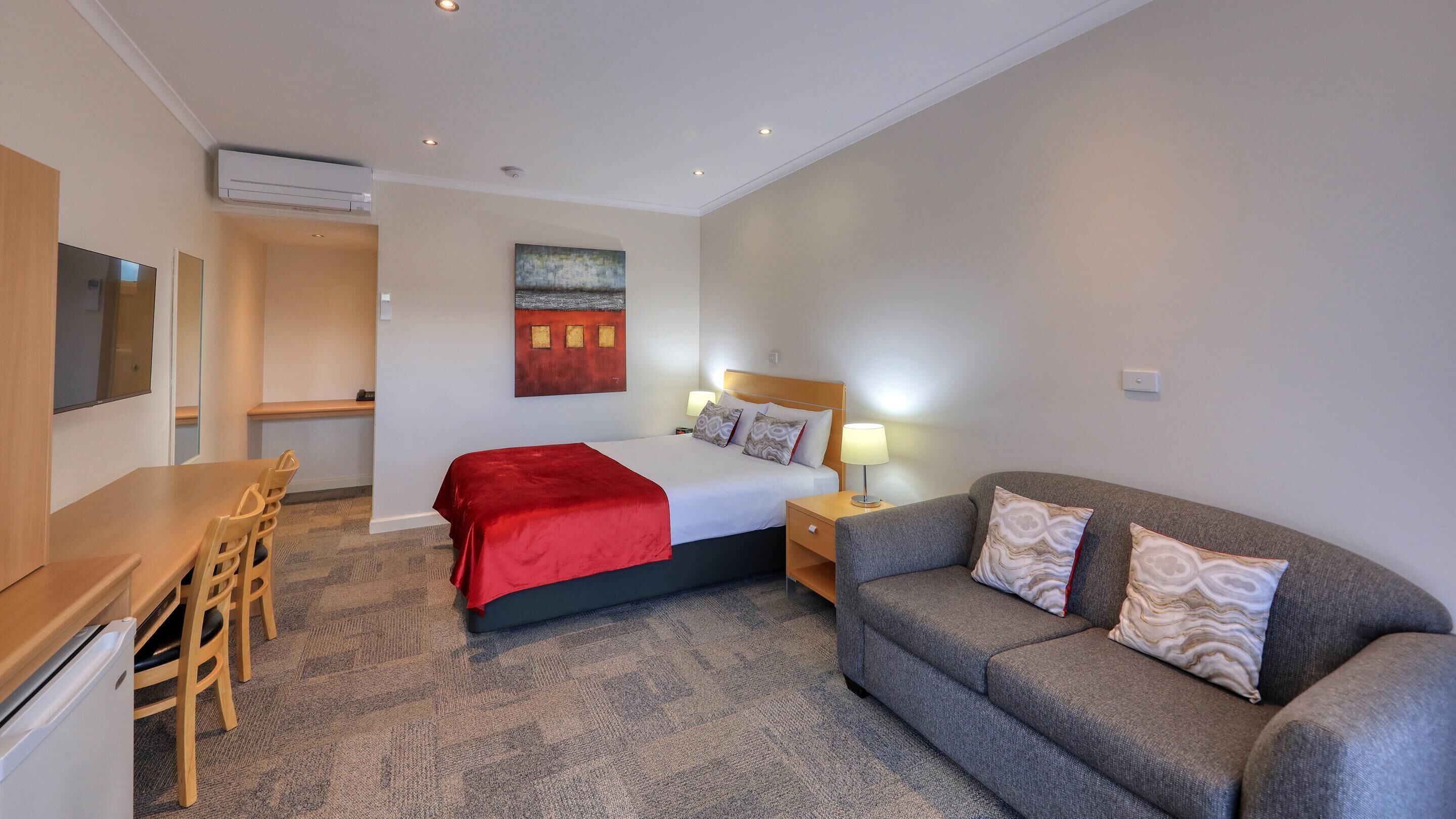 A hotel room with a bed, a sofa, a desk, and a chair.