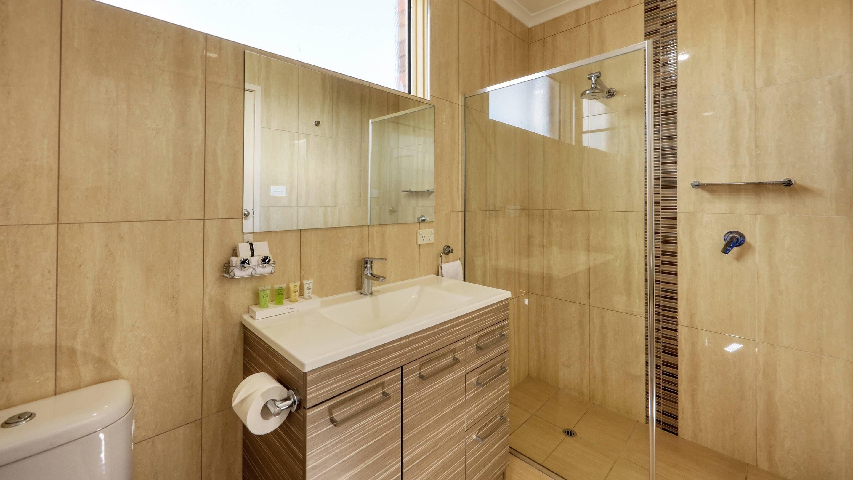 A bathroom with a large mirror, a sink, a toilet, and a shower area.