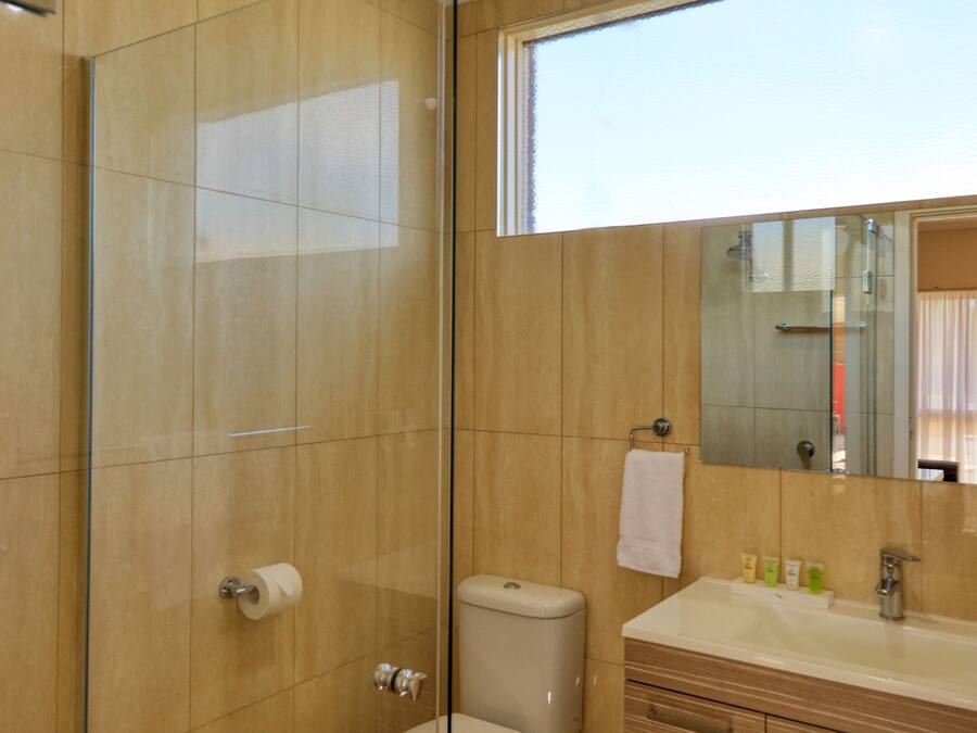 A bathroom with a glass shower enclosure, a toilet, a sink with toiletries, and a mirror.