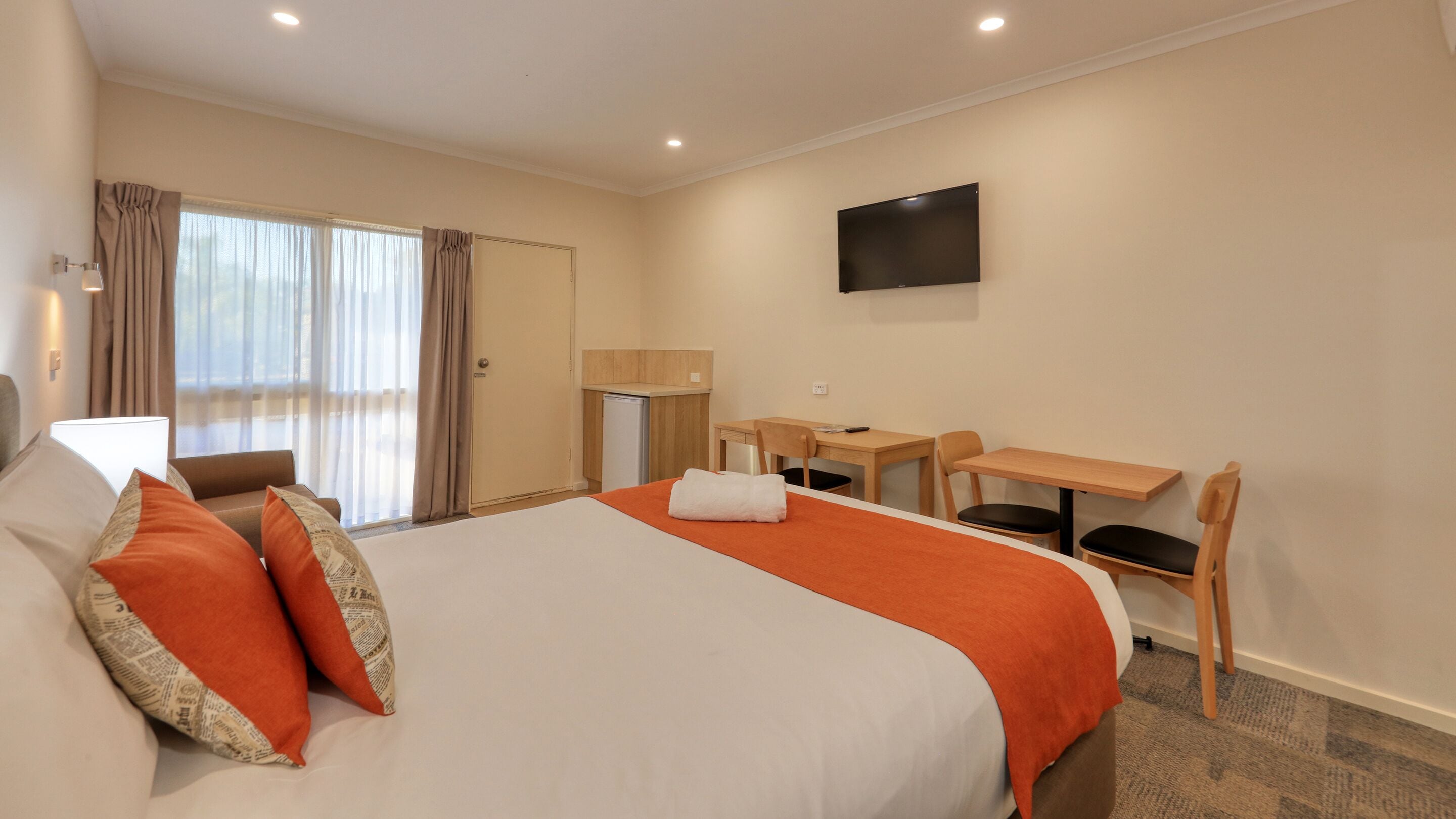 A hotel room with a large bed, a desk, a chair, a TV, and a window with curtains.