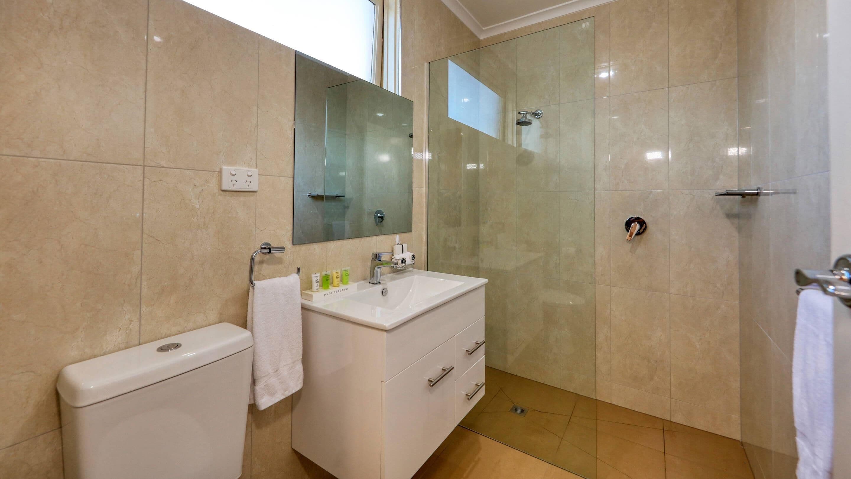 Ein Badezimmer mit Toilette, Waschbecken, Spiegel und Duschkabine aus Glas.