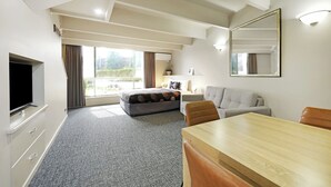 Una habitación de hotel moderna con un ventanal grande, un televisor de pantalla plana, un sofá, una mesa de comedor y un espejo.