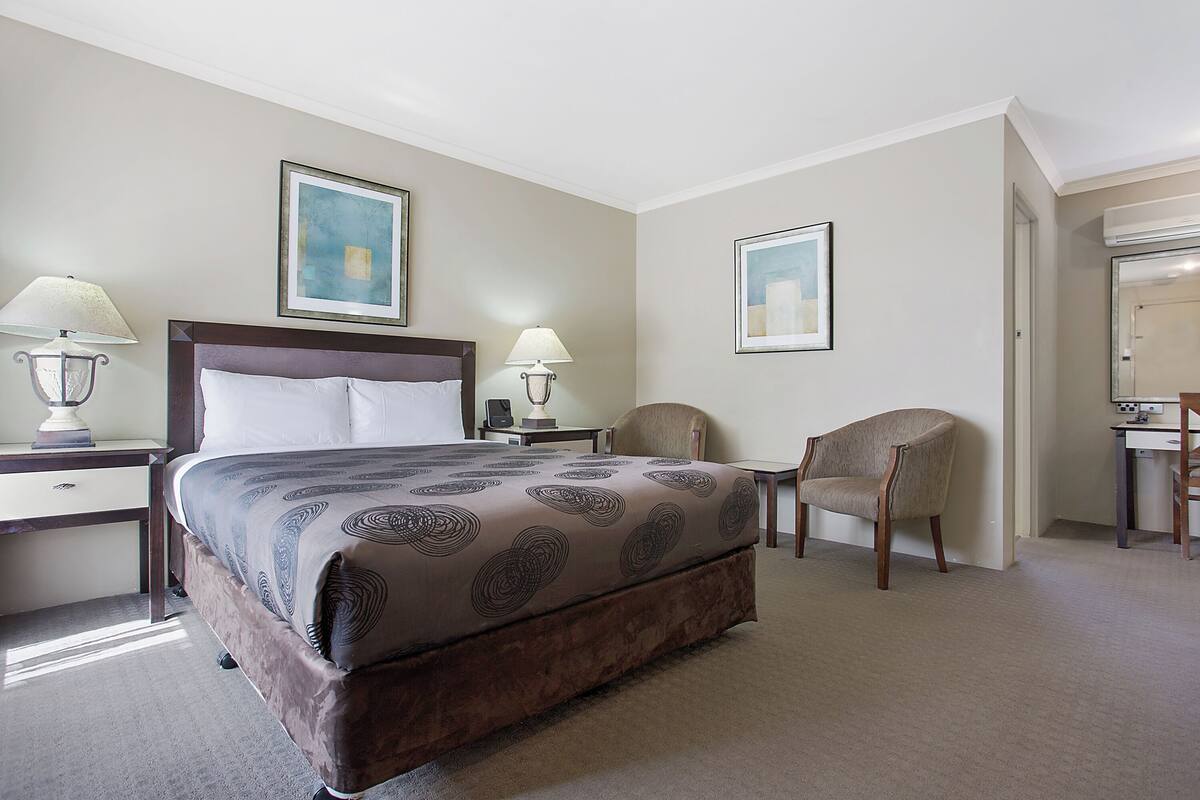 A hotel room with a large bed, two bedside tables with lamps, a chair, and two framed pictures on the walls.