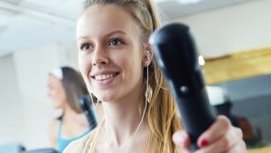 Una persona usando una máquina de ejercicios en un gimnasio, con otra persona al fondo.