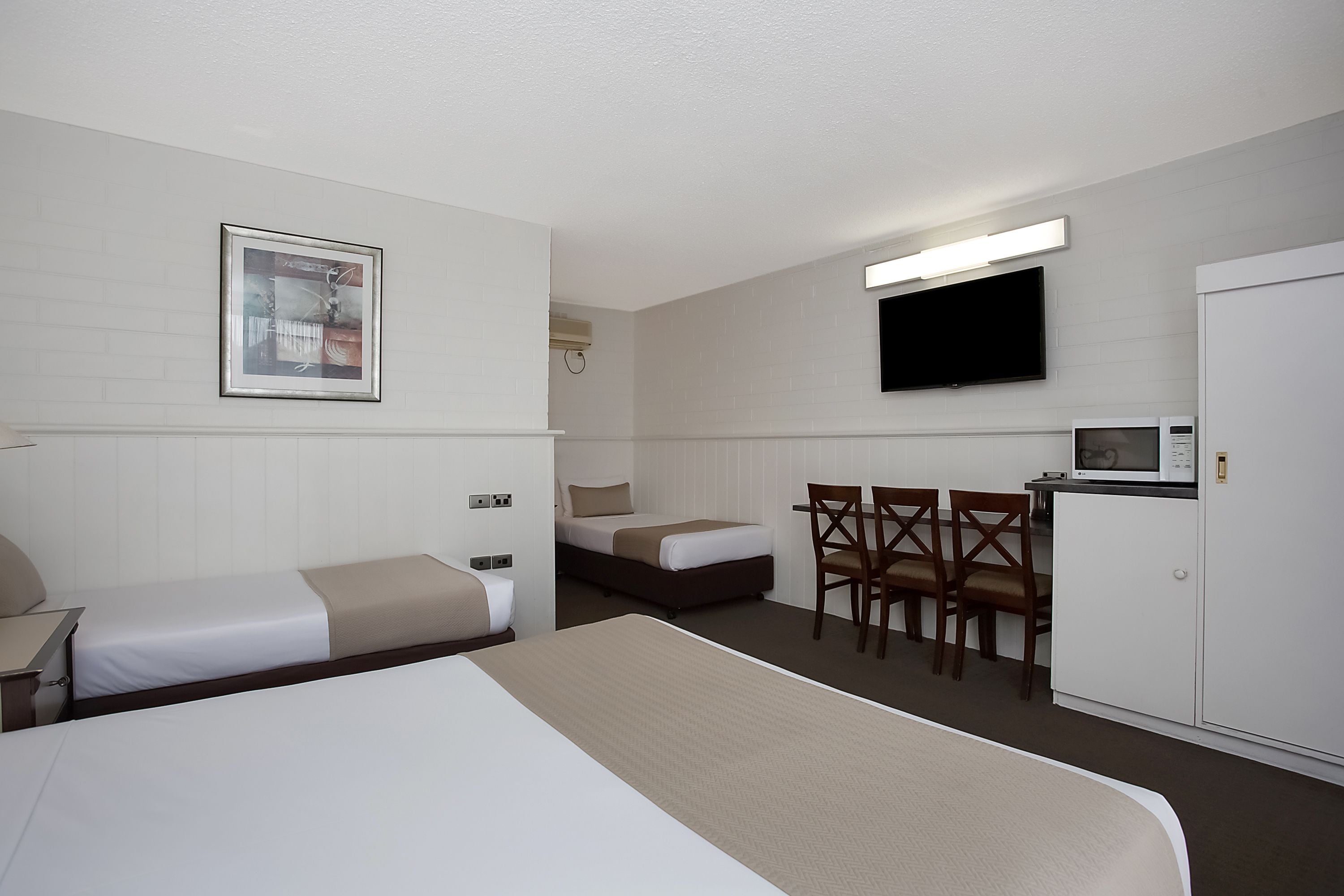 A hotel room with two beds, a desk, a chair, a television, and a microwave.