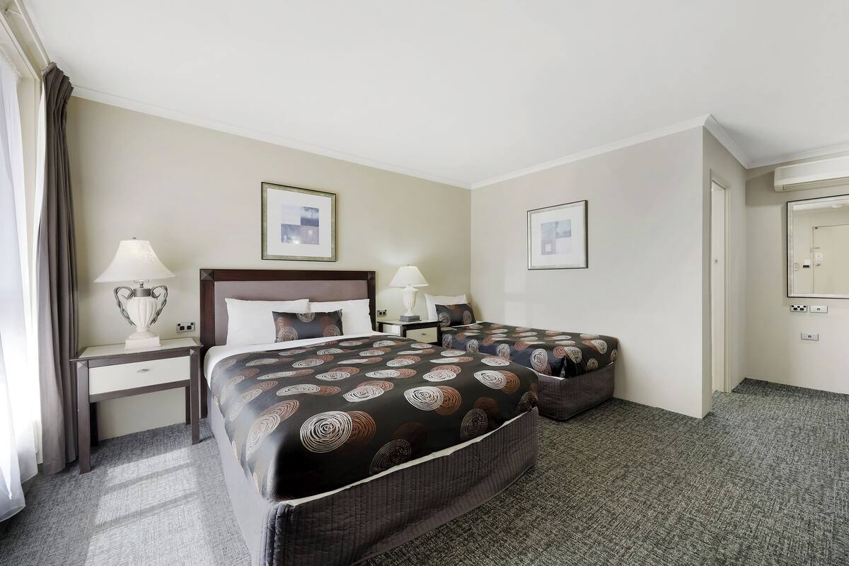 A hotel room with two beds, a nightstand, a lamp, and framed pictures on the wall.