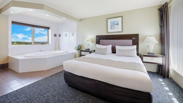 Habitación de hotel con una cama grande, baño privado con bañera y vista al cielo.