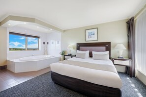A hotel room with a large bed, a separate bathroom with a bathtub, and a view of the sky.
