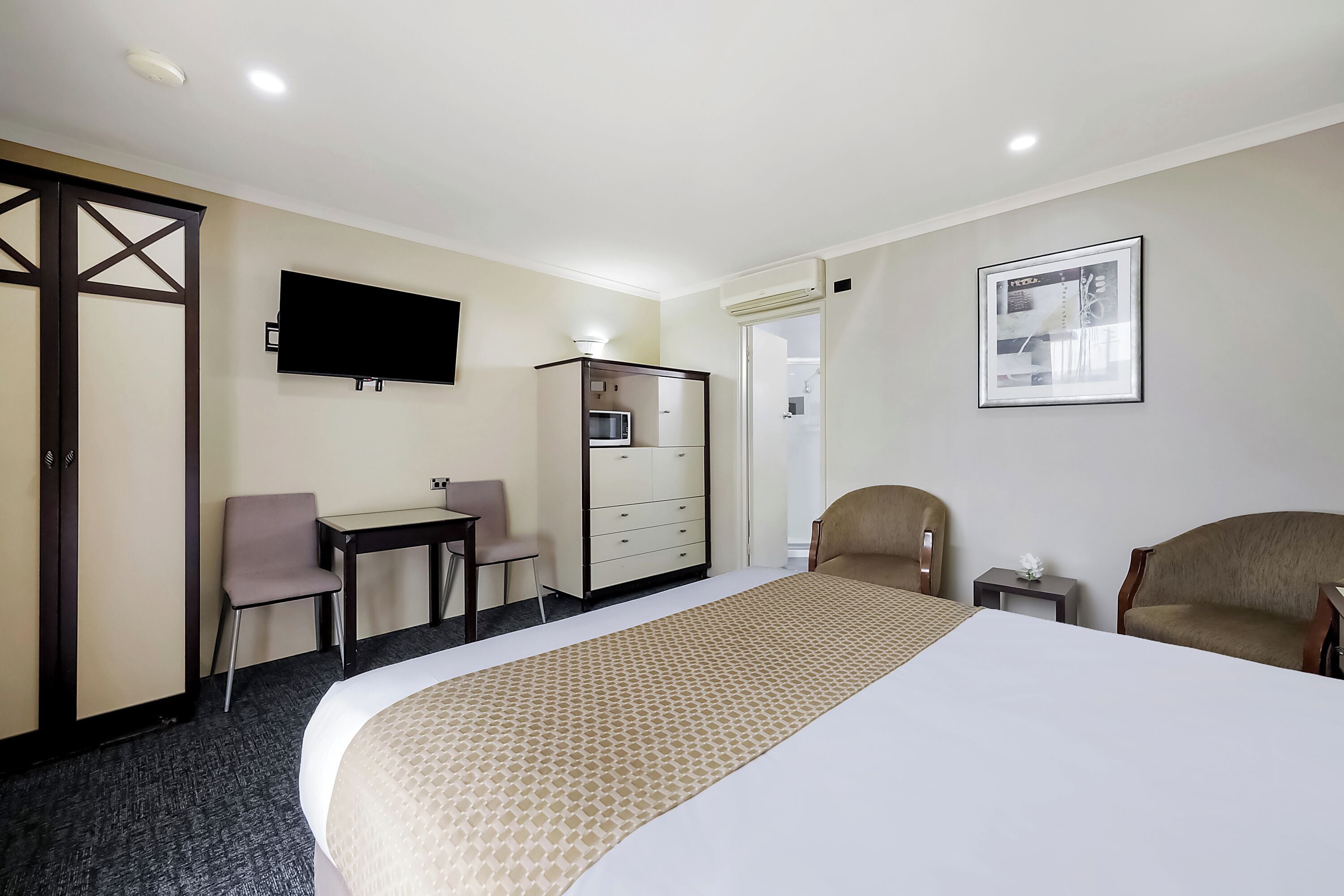 A hotel room with a bed, a desk, a chair, a TV, a dresser, and an air conditioning unit.