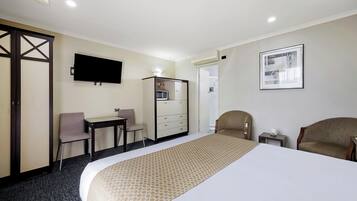 A hotel room with a bed, a desk, a chair, a TV, a dresser, and an air conditioning unit.
