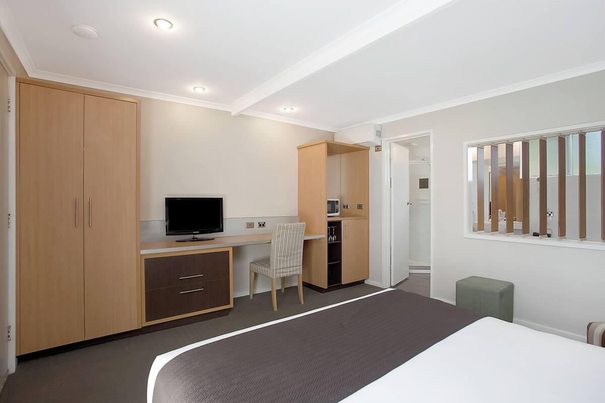A bedroom with a bed, a desk, a chair, a television, and a wardrobe.