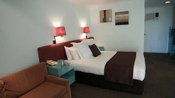 A hotel room with a bed, two bedside lamps, a telephone, a brown couch, and a teal nightstand.