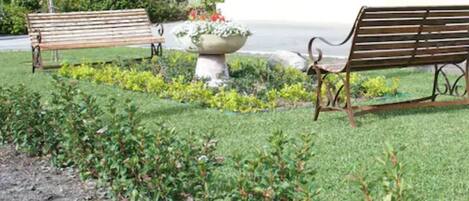 Two wooden benches in a garden with a planter and a grassy area.