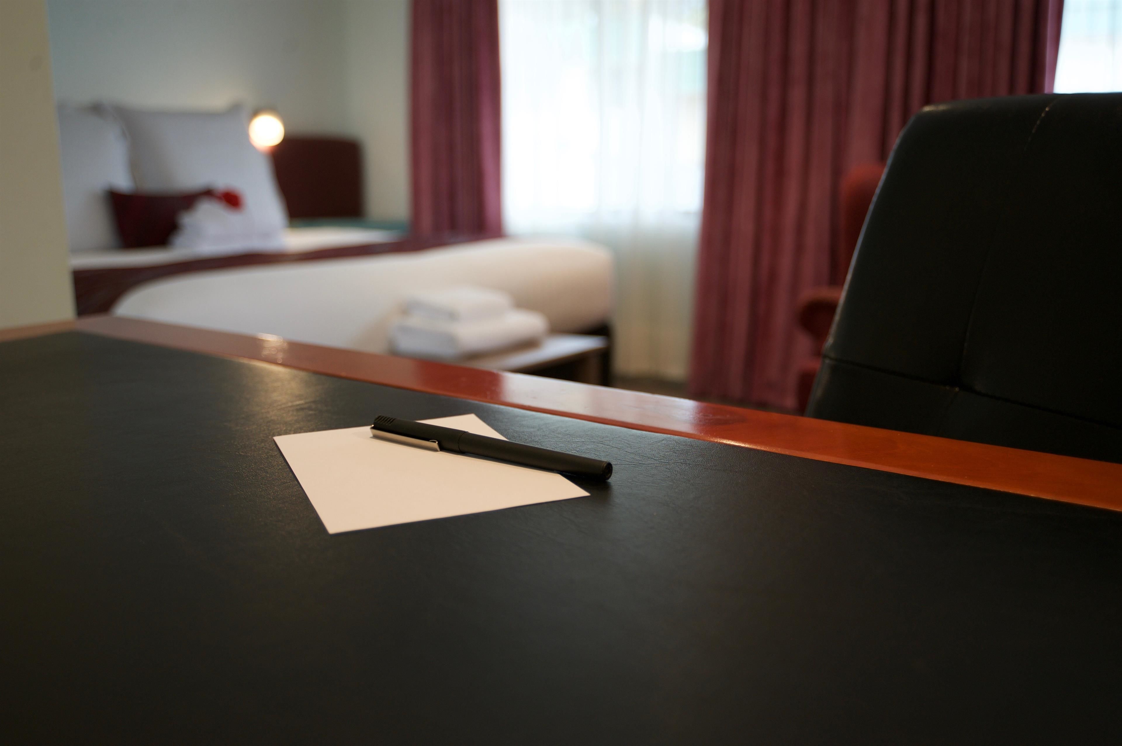 Una habitación de hotel con una cama, un escritorio con bolígrafo y papel, y una silla.