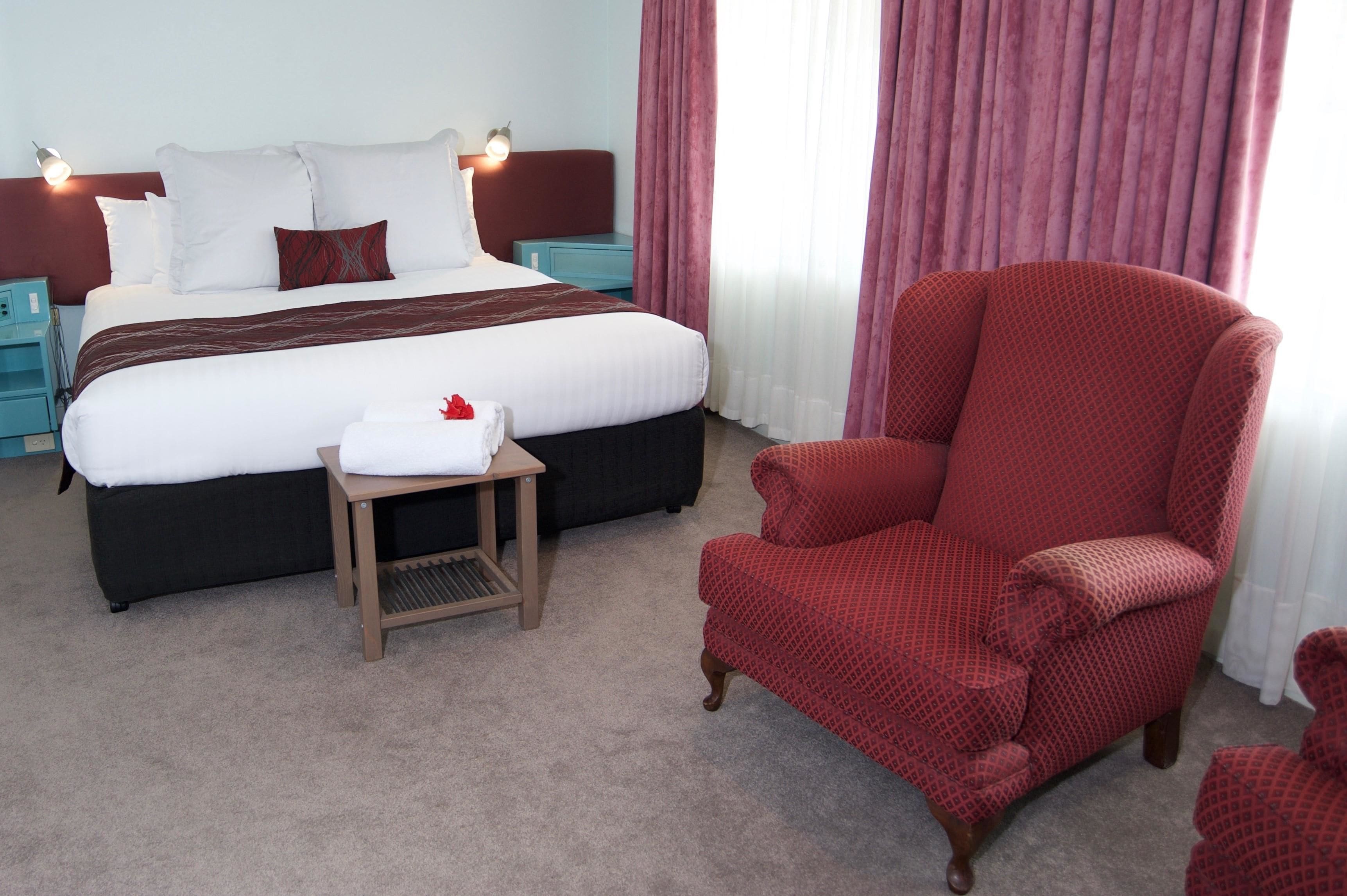 Ein Hotelzimmer mit einem großen Bett, einem roten Sessel, einem kleinen Tisch und einem Nachttisch.