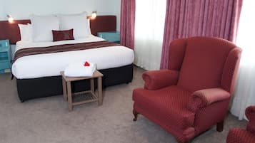 Een hotelkamer met een groot bed, een rode fauteuil, een klein tafeltje en een nachtkastje.